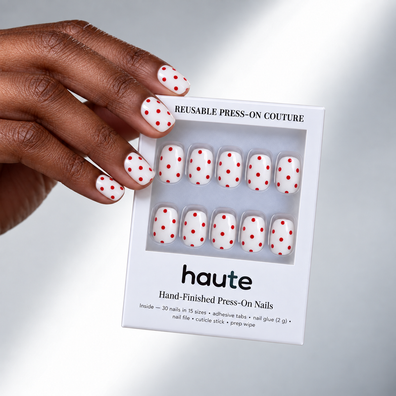 sweet spot super short square white and red polka dot press-on nails worn while holding the haute box