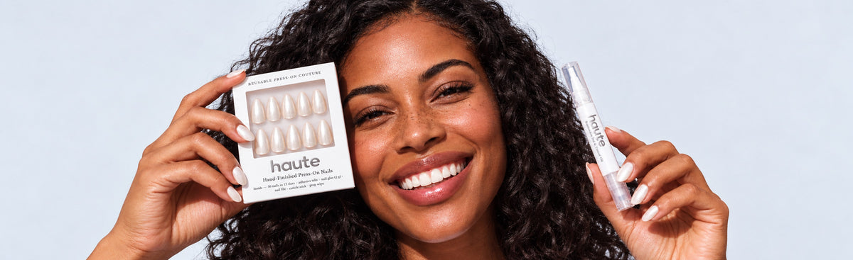 Smiling model holding a haute press-on nail set and cuticle oil pen